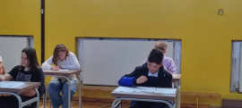Uczniowie siedzą przy stolikach i rozwiązują konkursowe zadania z matematyki 