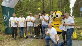Grupa mężczyzn w sportowych strojach. Wśród nich znajduje się duża maskotka pszczoły i kobieta w mundurze leśnika