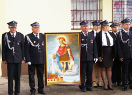 Mężczyźni i kobieta w mundurach strażackich. Dwaj mężczyźni trzymają obraz św. Floriana