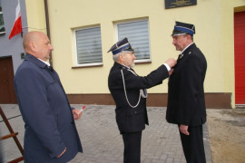 Trzech mężczyzn. Jeden wpina w klapę marynarki odznaczenie.