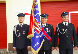 Trzech mężczyzn w mundurach. Jeden z nich trzyma sztandar