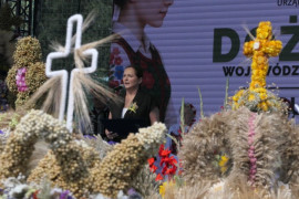 Kobieta przemawia na scenie, przed którą stoją wieńce dożynkowe 