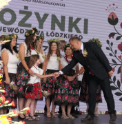 Grupa osób na scenie. Mężczyzna gratuluje małej dziewczynce 