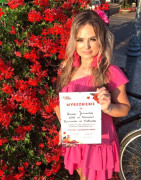 Kobieta w różowym stroju. Anna Janocha trzyma w ręku dyplom - wyróżnienie 