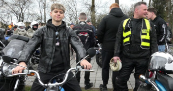 Chłopiec siedzi na motocyklu. Obok niego stoi mężczyzna 