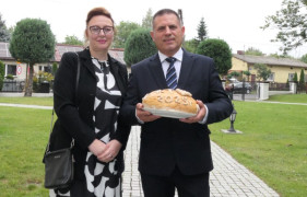 Kobieta i mężczyzna stoją obok siebie. Mężczyzna trzyma w dłoniach bochen dożynkowego chleba