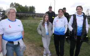 Kobity i mężczyźni stoją obok siebie. Za nimi znajduje się most kolejowy