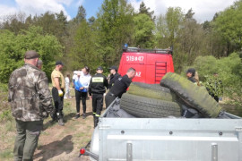 Grupa osób, samochód straży oraz przyczepka, na której znajdują się śmieci