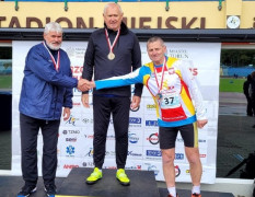 Trzej mężczyzn stoi na podium. Dwóch z nich podaje sobie dłonie