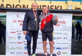 Dwaj mężczyźni na podium. Jeden z nich podnosi rękę w geście triumfu 
