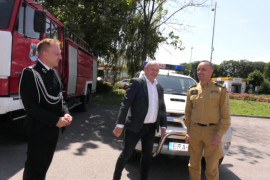 Trzej mężczyźni stoją obok siebie. Widoczne są samochody straży pożarnej 
