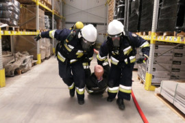 Dwaj strażacy wynoszą poszkodowaną osobę z budynku 