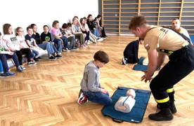 Grupa dzieci i strażacy. Strażacy tłumaczą dzieciom zasady udzielania pierwszej pomocy