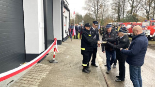 Osoby stoją przed budynkiem garażowym OSP Dąbrówka. Za chwilę nastąpi przecięcie wstęgi