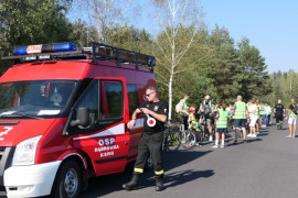 Samochód strażacki i grupa osób jadąca rowerami 