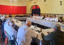 Grupa osób na spotkaniu. Osoby siedzą za stołem. 