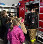 Dzieci w towarzystwie osoby dorosłej oglądają bojowy wóz strażacki 