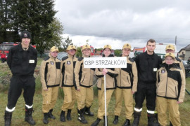 Strażacy OSP Strzałków stoją obok siebie. Jeden z nich trzyma transparent 