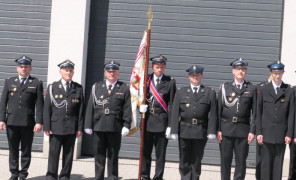 Strażacy w mundurach. Jeden z nich trzyma sztandar 