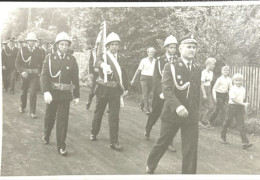 Mężczyźni w strażackich strojach idący defiladowym krokiem ulicą 