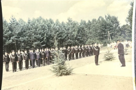 Grupa osób w szeregu. Dwóch mężczyzn w mundurach stoi naprzeciwko siebie