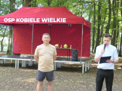 Dwaj mężczyźni stoją obok siebie. Jeden z nich trzyma w ręku mikrofon 