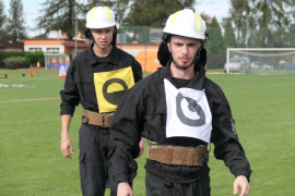 Druhowie OSP Strzałków idący po murawie stadionu 
