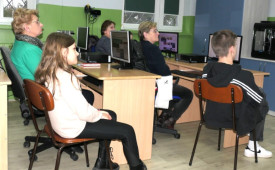Dorośli i dzieci siedzą obok siebie w szkolnych ławkach 