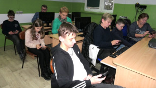 Dorośli i dzieci siedzą na krzesłach. Wszyscy trzymają w dłoniach smartfony