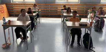 Dzieci siedzą w szkolnych ławkach 