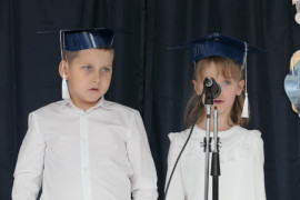 Dziewczynka i chłopiec stoją obok siebie. Na głowach mają granatowe birety