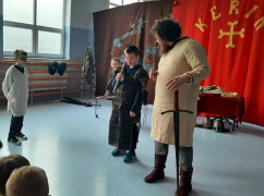 Mężczyzna i dwóch chłopców. Wszyscy ubrani są w historyczne stroje. Trwa pokazowa lekcja walk za czasów pierwszych Piastów 