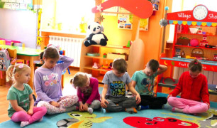 Dzieci podczas zajęć ruchowych. Maluchy siedzą na dywanie w sali lekcyjnej 