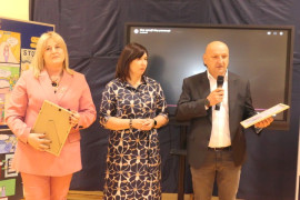 Dwie kobiety i mężczyzna stoją obok siebie. Mężczyzna trzyma w dłoniach dyplom 
