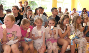 Dzieci siedzą obok siebie i jedzą lody