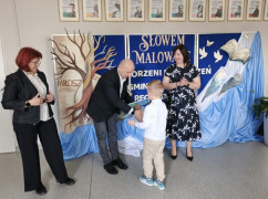 Dwie kobiety i mężczyzna oraz mały chłopiec. Wszyscy stoją obok siebie. Mężczyzna wręcza chłopcu dyplom 