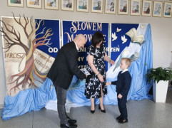 Kobieta i mężczyzna oraz mały chłopiec stoją obok siebie. Mężczyzna wręcza chłopcu dyplom 