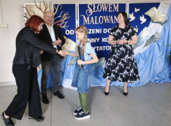 Dwie kobiety, mężczyzna i dziewczynka stoją obok siebie. Kobieta wręcza dziewczynce dyplom 