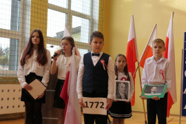 Uczniowie w galowych strojach podczas akademii z okazji Narodowego Święta Niepodległości. Widoczne są biało - czerwone flagi