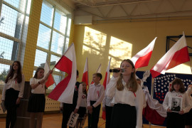 Uczniowie w galowych strojach podczas akademii z okazji Narodowego Święta Niepodległości. Widoczne są biało - czerwone flagi