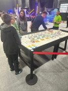Grupa osób znajdujących się przy stole, na którym rozłożone są klocki lego