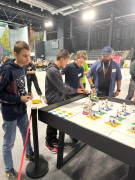 Grupa osób stojąca przy stole, na którym znajdują się klocki lego