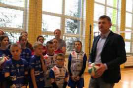 Grupa dzieci w sportowych strojach i mężczyzna trzymający w ręku piłkę 