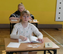 Dziewczynka siedzi w ławce. W dłoniach trzyma książkę 