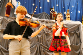Dwie dziewczynki: jedna gra na skrzypcach, druga trzyma w ręku mikrofon i śpiewa 