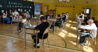 Uczniowie siedzą w ławkach i rozwiązują test konkursowy 