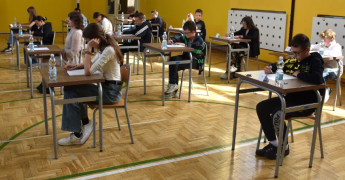 Uczniowie siedzą w ławkach i rozwiązują tekst w ramach konkursu