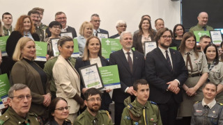 Grupa osób stoi obok siebie. Niektóre z nich trzymają w dłoniach zielone tabliczki 