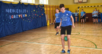 Grupa dzieci w niebieskich bluzkach podczas zawodów sportowych. Chłopiec podbija piłkę