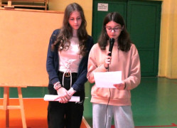 Dwie uczennice stoją obok siebie. Jedna z nich przemawia przez mikrofon 